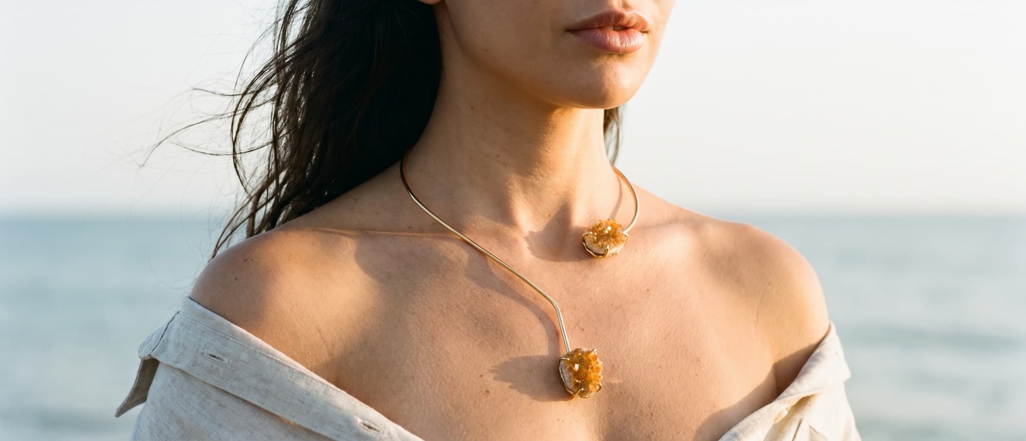 Choker de aro dourado aberto, com as duas drusas de citrino do mesmo lado, à beira-mar no fim da tarde