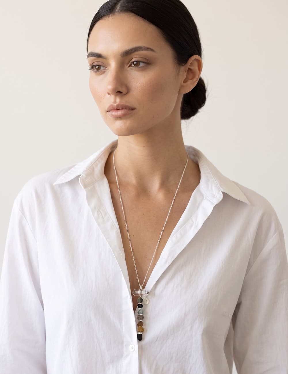 Colar 7 Chakras prateado sobre camisa branca aberta, as sete pedras e a ponta de cristal no peito