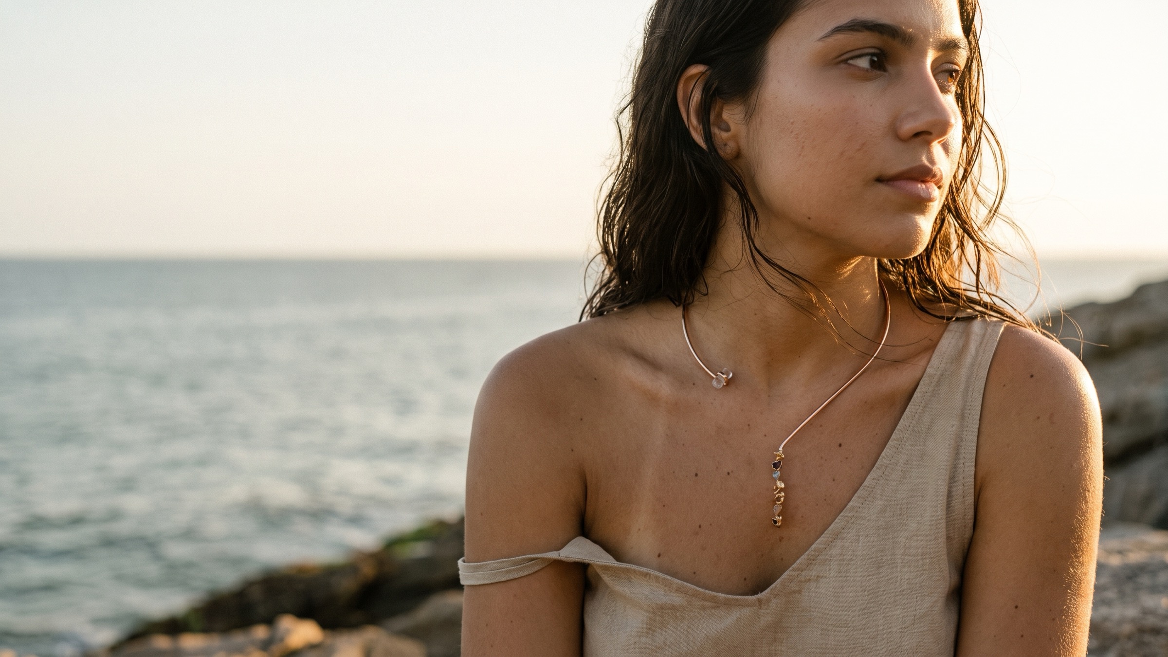 Modelo à beira-mar no fim da tarde usando o choker 7 Chakras, com a cascata de pedras sobre o colo